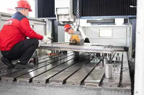 Osm Press Brake Manufacturing Process: Skilled Assembly Team Collaborating to Secure Base Frame Components, Demonstrating Precision Assembly Techniques and Teamwork in High-End CNC Equipment Production, Showcasing Osma's Expertise in Metal Fabrication Mac