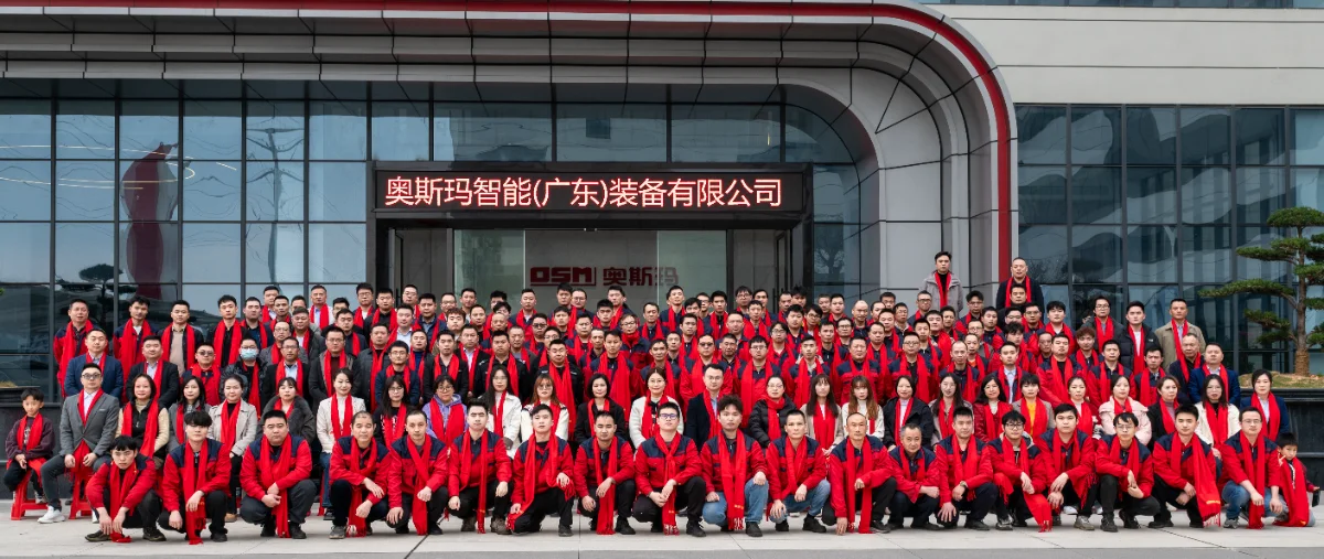 A large group photo of OSM (OSM Intelligent (Guangdong) Equipment Co., Ltd.) employees gathered outside the company headquarters for the 2026 Annual Meeting on January 31, 2026. The team is dressed in matching red scarves and jackets, symbolizing unity an