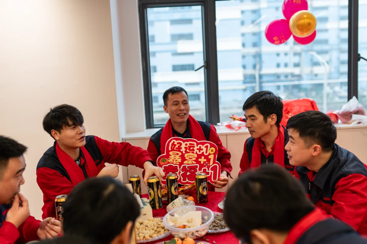 OSM employees celebrate the 2026 Annual Meeting with festive red attire and snacks. The team gathers around a table, enjoying a moment of unity and camaraderie during the company's milestone event.