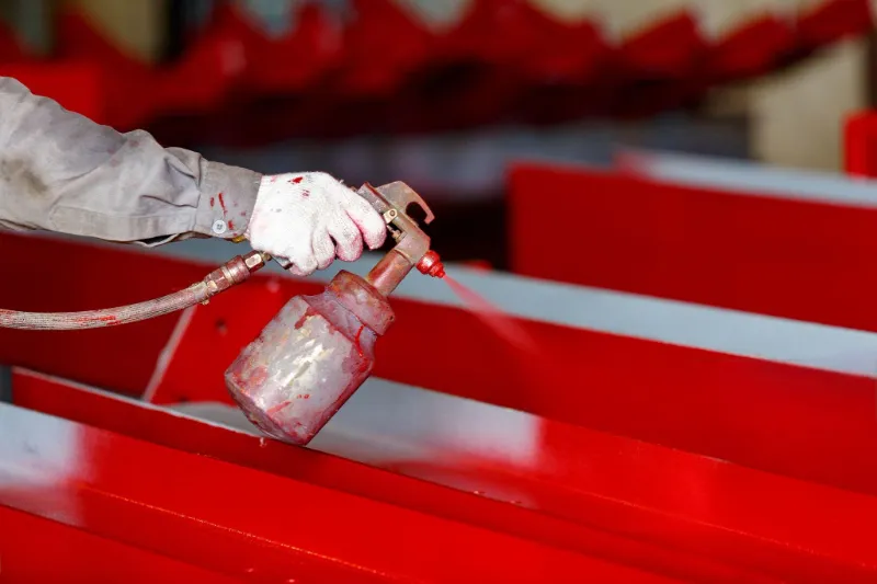 OSM manufacturing process painting scene, worker spraying eco-friendly red paint on machine body, showcasing high-quality coating process.